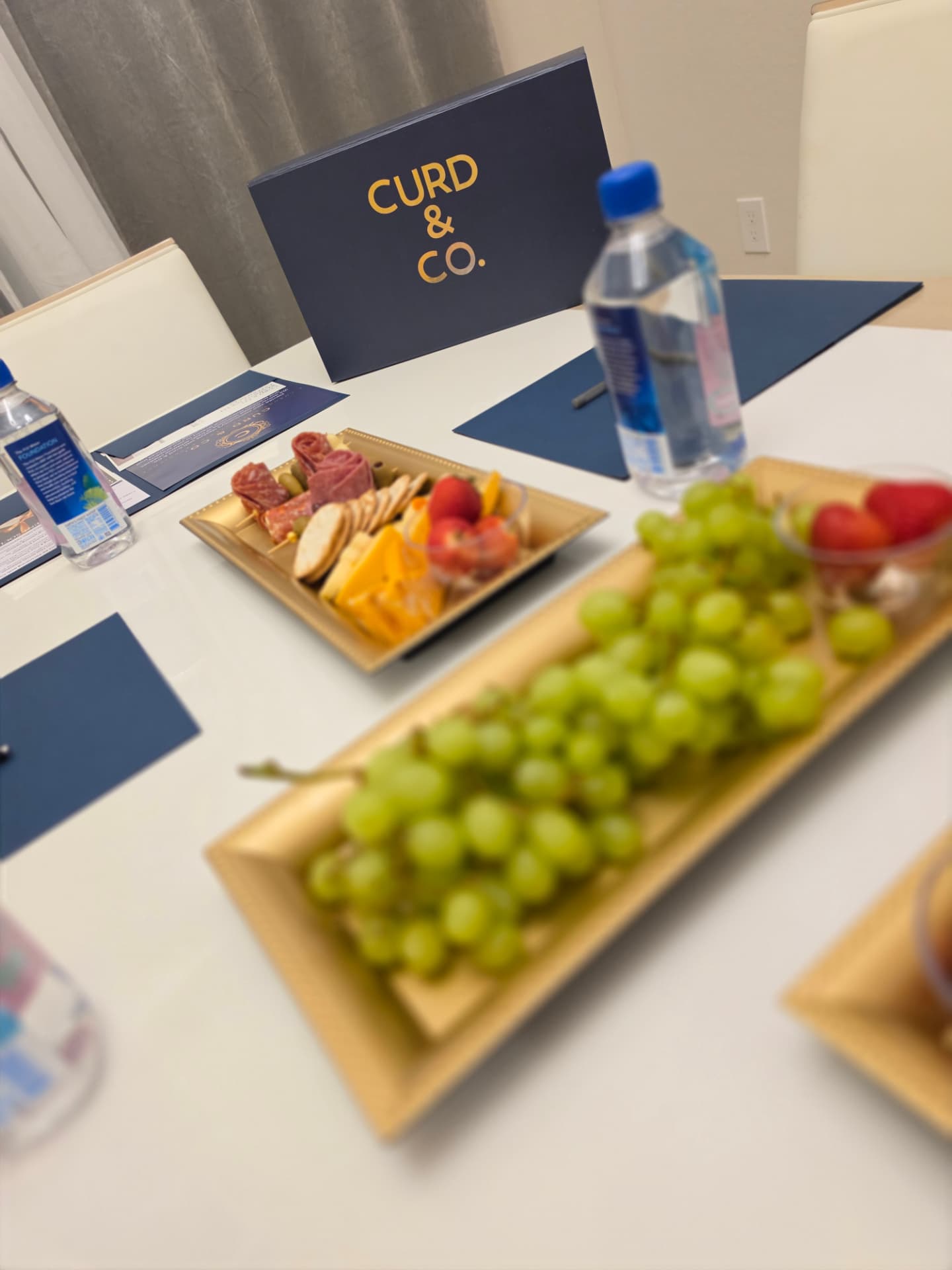 Branded Curd & Co. card on a conference table with gold trays of charcuterie and grapes