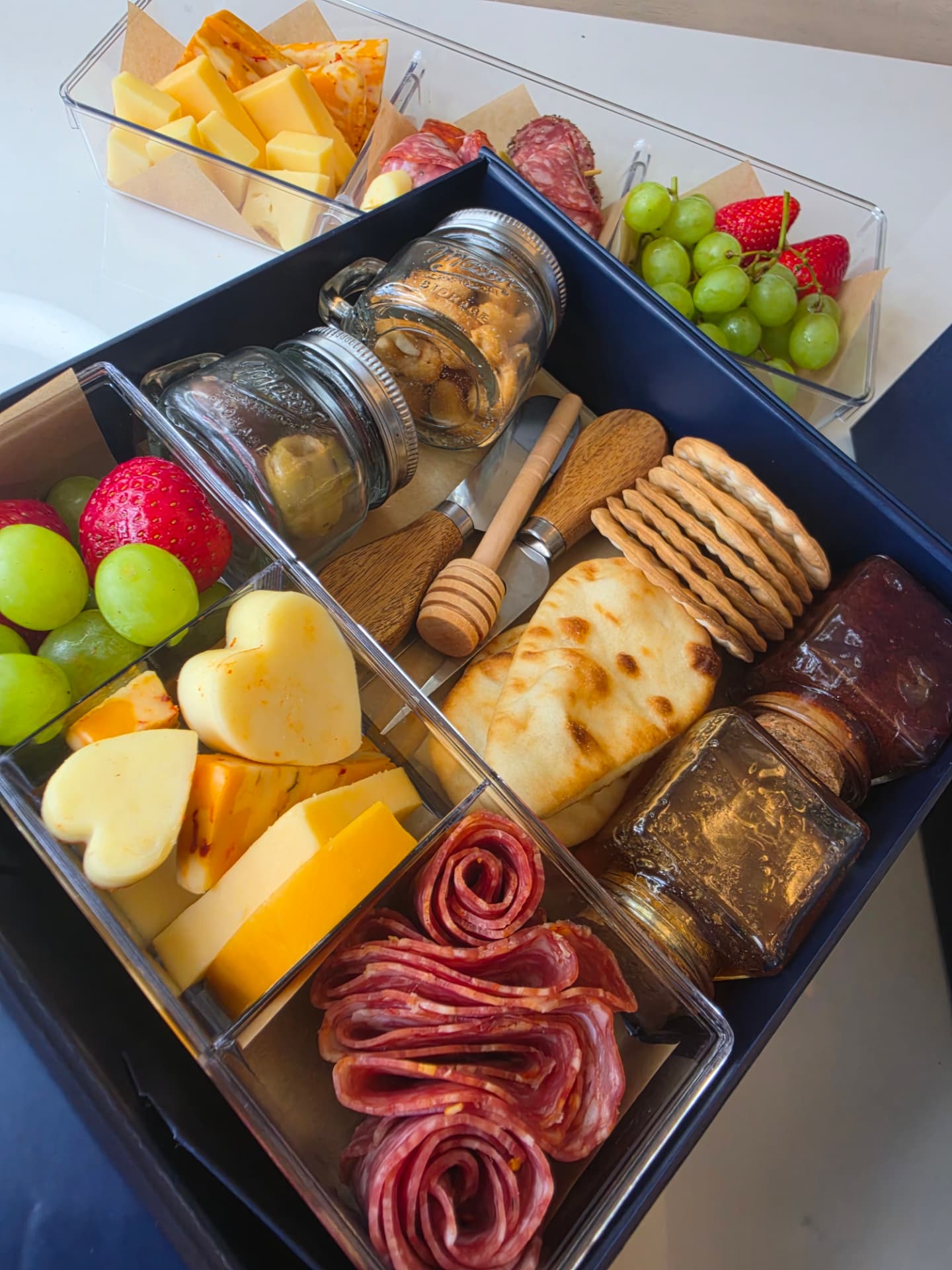 Open charcuterie box with heart-cut cheeses, salami roses, naan and preserves