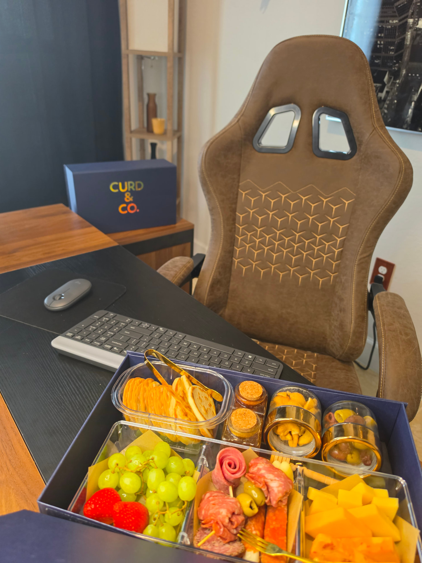 Curd & Co. box open on an executive desk with cheeses, salami and preserves