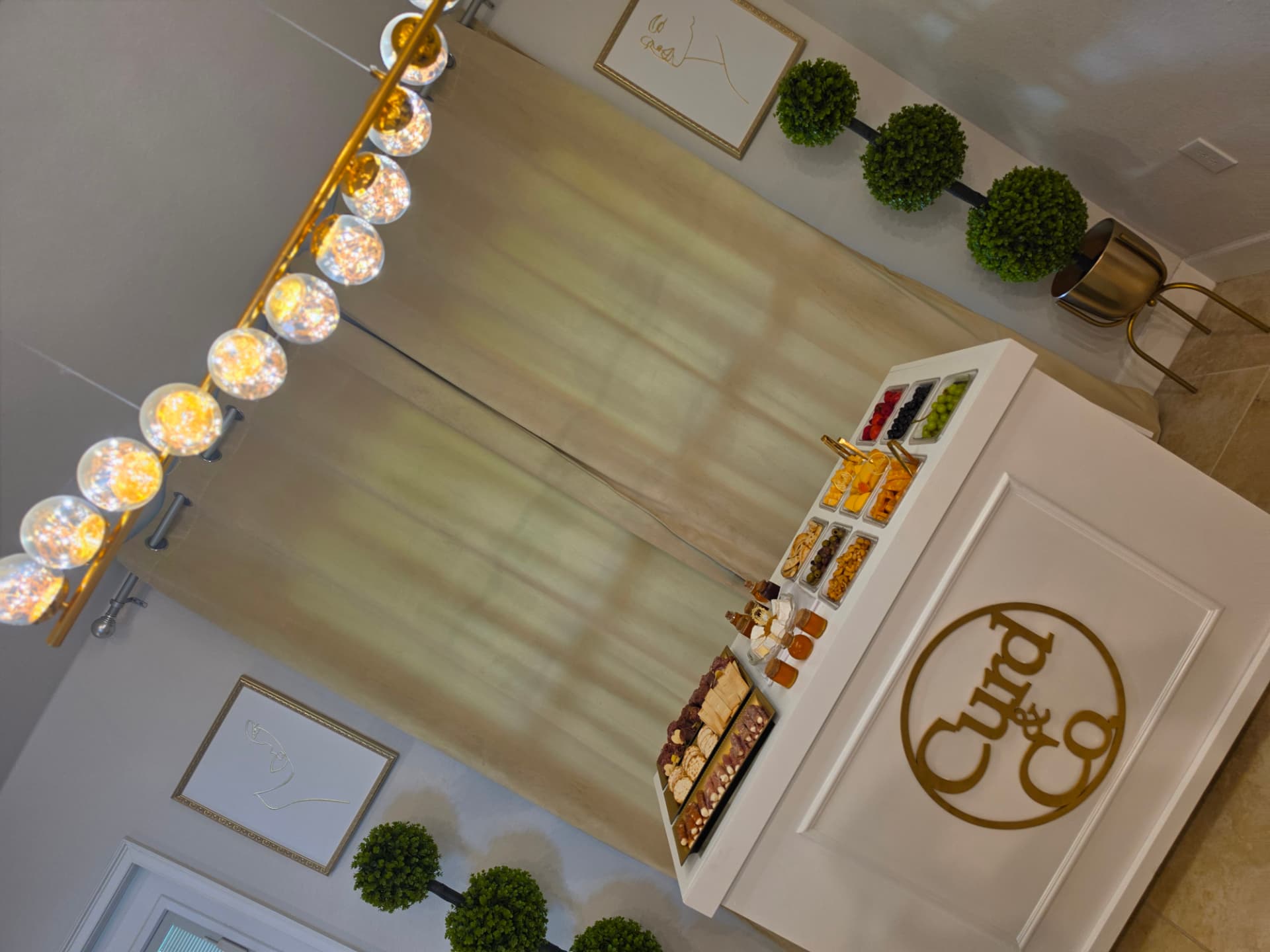 Mobile charcuterie bar styled indoors with draping, topiaries and globe lighting