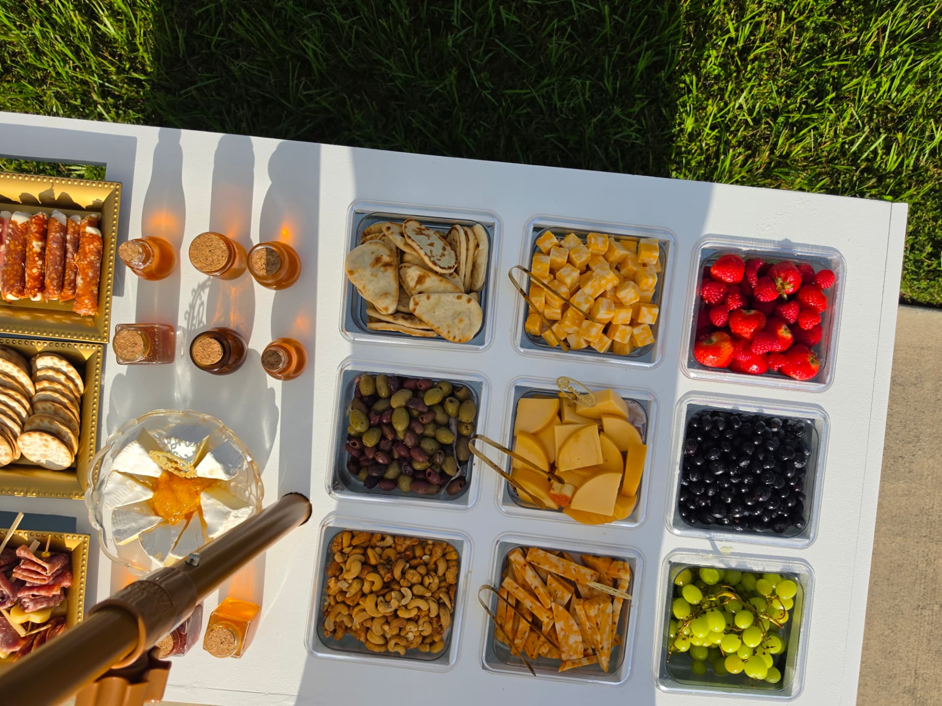 Overhead view of a white bar top with trays of naan, cheeses, olives, nuts, strawberries, blueberries and grapes beside honey jars and baked brie