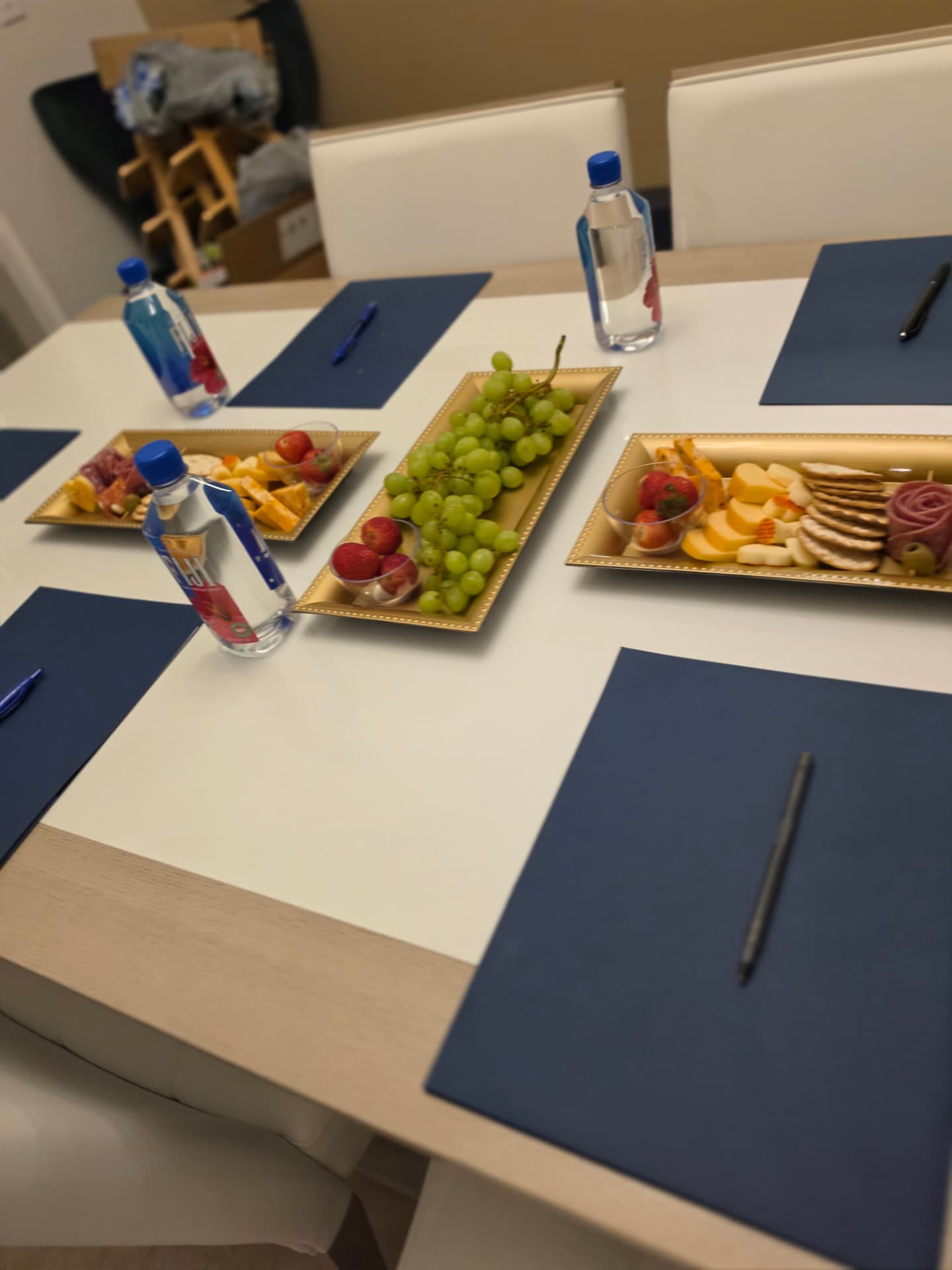 Conference table set with navy placemats and gold trays of cheese, meats and fruit