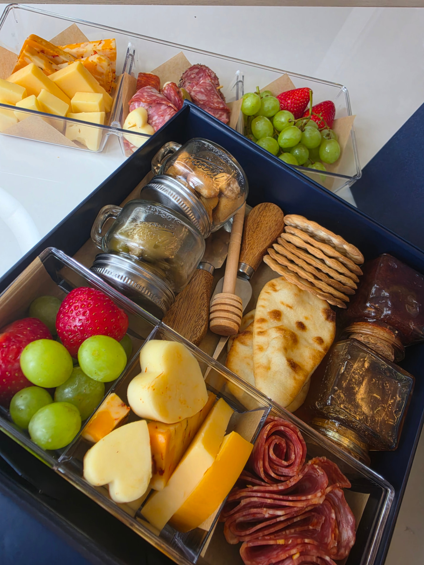 Overhead view of an open charcuterie box with cheeses, salami, naan, crackers and jars